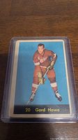 Front image of Gordie Howe in hockey pose on blue background, showing some wear and discoloration.