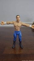 Front view of WWE Chris Benoit wrestling action figure with arms extended showing muscular torso and blue tights.