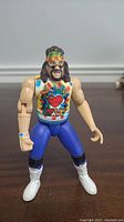 Front view of WWE Dude Love Mick Foley action figure showing detailed face, headband, tie-dye shirt with Dude Love logo, blue pants and white boots.