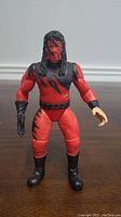 Front view of WWE Kane action figure showing red and black detailed wrestling outfit, mask, and black hair.