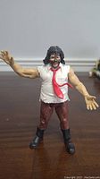 Front view of WWE Mankind Mick Foley figure standing on wooden surface, showing detailed clothing and face paint.