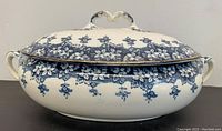 Oval vintage blue and white soup bowl with lid, decorated with a blue floral pattern and gold rim, and two side handles for carrying.