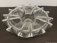 Clear glass depression dish side angled view showing textured and multifaceted design with raised points along edge and pedestal base.