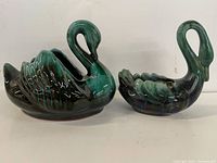 Two blue mountain pottery swan figurines with curved necks and glossy green-black glaze.