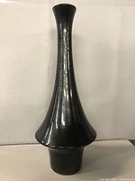 Full side view of tall black ceramic vase showing its flared lower middle section and slim neck.