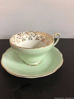 Side photo showing light green bone china tea cup with gold floral pattern inside the cup and gold trim on handle and rim.