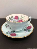 Tea cup and saucer showing pink roses, green leaves, scalloped edges with gold trim