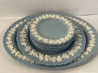 Stack of Wedgwood blue Jasperware dishes including small, medium, and large round plates with white grapevine relief decoration on the rims, showing fluted edges