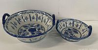 Two blue and white ceramic bowls with side handles and decorative blue floral patterns on white base placed side by side