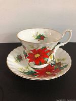 Tea cup and saucer set with vivid poinsettia and holly design on white bone china, showing gold trim and details