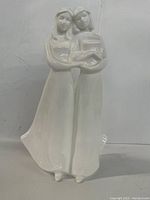 Front and side view of white porcelain figurine showing two women standing close with arms linked.