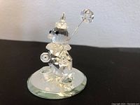 Clear faceted Swarovski crystal clown figurine positioned on a round glass base, showing the side with balloon and detailed crystal body.
