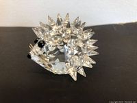 Side angled view of Swarovski crystal hedgehog showing clear faceted crystal body with multiple pointed crystal spikes and black eyes and nose accents