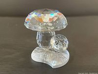 Front view of clear faceted Swarovski crystal mushroom figurine with a smaller mushroom attached to the side, showing the prismatic light reflections and detailed base.
