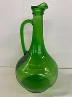 Front and side views of the vintage green glass decanter showing its shape, handle, and curved spout.