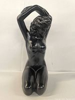 Front view of black kneeling woman figurine with arms raised and hands clasped behind head