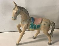 Side view of the painted wooden horse figurine showing detailed carved features and colorful saddle and harness.