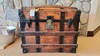Front view of an antique wooden trunk with black metal reinforcements and central lock.