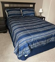 Full size bed dressed with blue and gray striped bedding set including comforter and pillows.