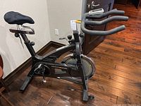 Full side view of bike on hardwood floor showing frame, seat, handlebars and flywheel