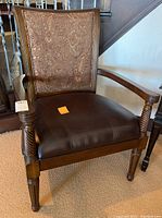 Front view of one armchair showing leather seat and paisley fabric back with carved wooden frame and armrests.