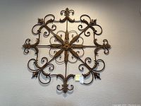 Front view of large metal wall art mounted on a light-colored wall, showing the entire piece with a square shape and ornate scrollwork.