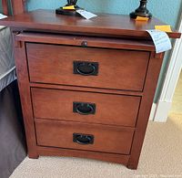 Front view of bedside chest showing three closed drawers with metal drop handles in Mission style.
