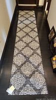 Full view of the runner rug laid out on dark hardwood floor showing black and white patterned design.