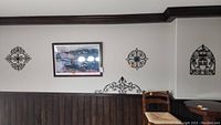 View of wall showing three black metal wall hangings mounted above dark wood paneling and a large framed Colorado Fourteeners print in center.