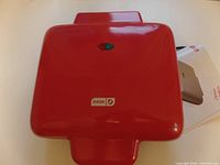 Closed red Dash mini waffle maker with indicator light and logo visible on top.