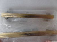 Close-up image of two gold drawer or cabinet pulls inside clear plastic packaging showing smooth rectangular profile and gold finish.