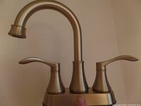 Front view of brushed gold faucet installed on deck plate showing gooseneck spout and two handles.