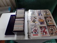 Photo of binder open with hockey cards in plastic sleeves and a box containing loose hockey cards stacked vertically.