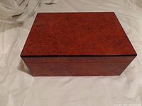 Closed view of humidor showing polished reddish-brown wood finish with distinct wood grain pattern on top surface and sides.