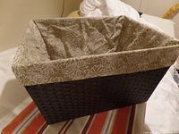 Front and top angle view of the rectangular dark brown woven paper rope basket with beige floral cotton lining folded over the edge.