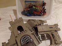 Playmobil castle components including walls and gate in gray plastic, displayed outside of box.