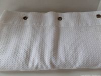 White waffle weave textured shower curtain spread out showing fabric pattern and rusted grommets.