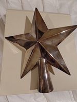 Front angled view of a silver plated five-point star Christmas tree topper showing tarnish and reflective surfaces.