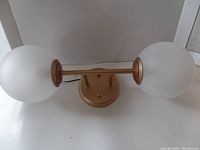 Image showing the full gold vanity light fixture with two frosted glass globes on each side of a central gold mounting plate and bar.