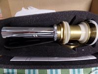 Pop-up drain body showing gold/brass threaded body with attached chrome overflow tube packed in foam inside box.