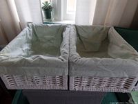 Two white wicker Ikea baskets side by side, showing interior cotton flannel liners draped over edges.