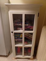 Front view of the white pine cabinet showing its glass paneled door and contents inside, including boxes and jars.