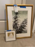 Full view of two framed woodblock prints, one large and one small, leaning against a wall on carpet