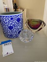 Three items on white surface: blue and white Williams Sonoma ceramic container, signed multi-color glass bowl, and clear crystal candle holder.