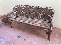 Full view of metal patio bench showing decorative backrest and seating slats