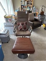 Front view of brown leather adjustable chair with matching footstool and decorative cushion in a beige and brown leaf floral pattern.