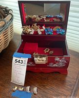 Overview of red lacquer jewelry box open on table showing various earrings and brooch plus items displayed in front