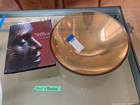 Photo showing the signed 16 inch amber-golden glass bowl with a MaxSold price tag and four art books including one on William Morris
