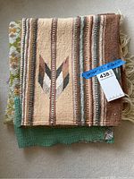Stack of Native American woven rug on top of quilt, showing pattern, texture, and attached lot tags