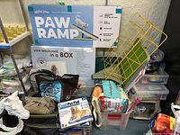Entire lot displayed on shelving including ramp box, pet loo box, playpen, cooling pad, carrier, diapers and other items